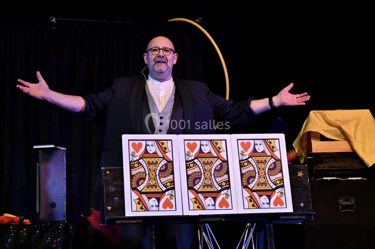 Un magicien présente un tour de cartes géantes sur une scène avec des accessoires en arrière-plan.