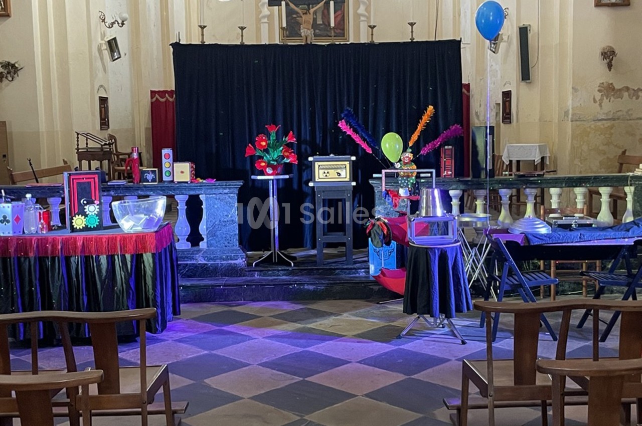 Scène colorée de spectacle de magie dans une salle avec rideau noir, accessoires et décorations lumineuses.
