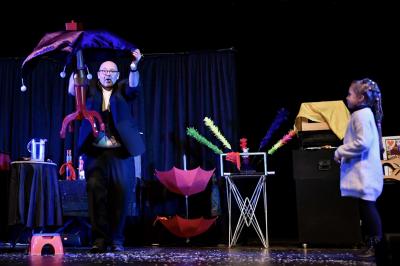 Scène de spectacle avec décorations festives, rideaux noirs, tables ornées et un sapin de Noël illuminé.