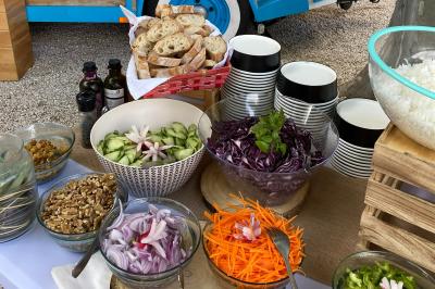 Buffet de salades avec légumes frais, noix, pain tranché et condiments, présenté en extérieur sur une table.