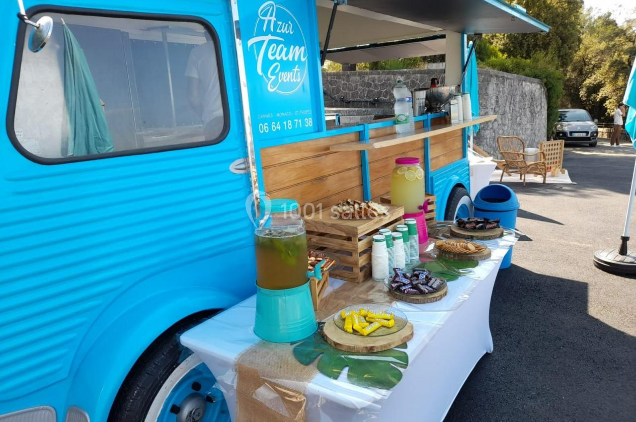 Stand mobile bleu proposant des boissons, desserts et collations disposés sur une table en extérieur.