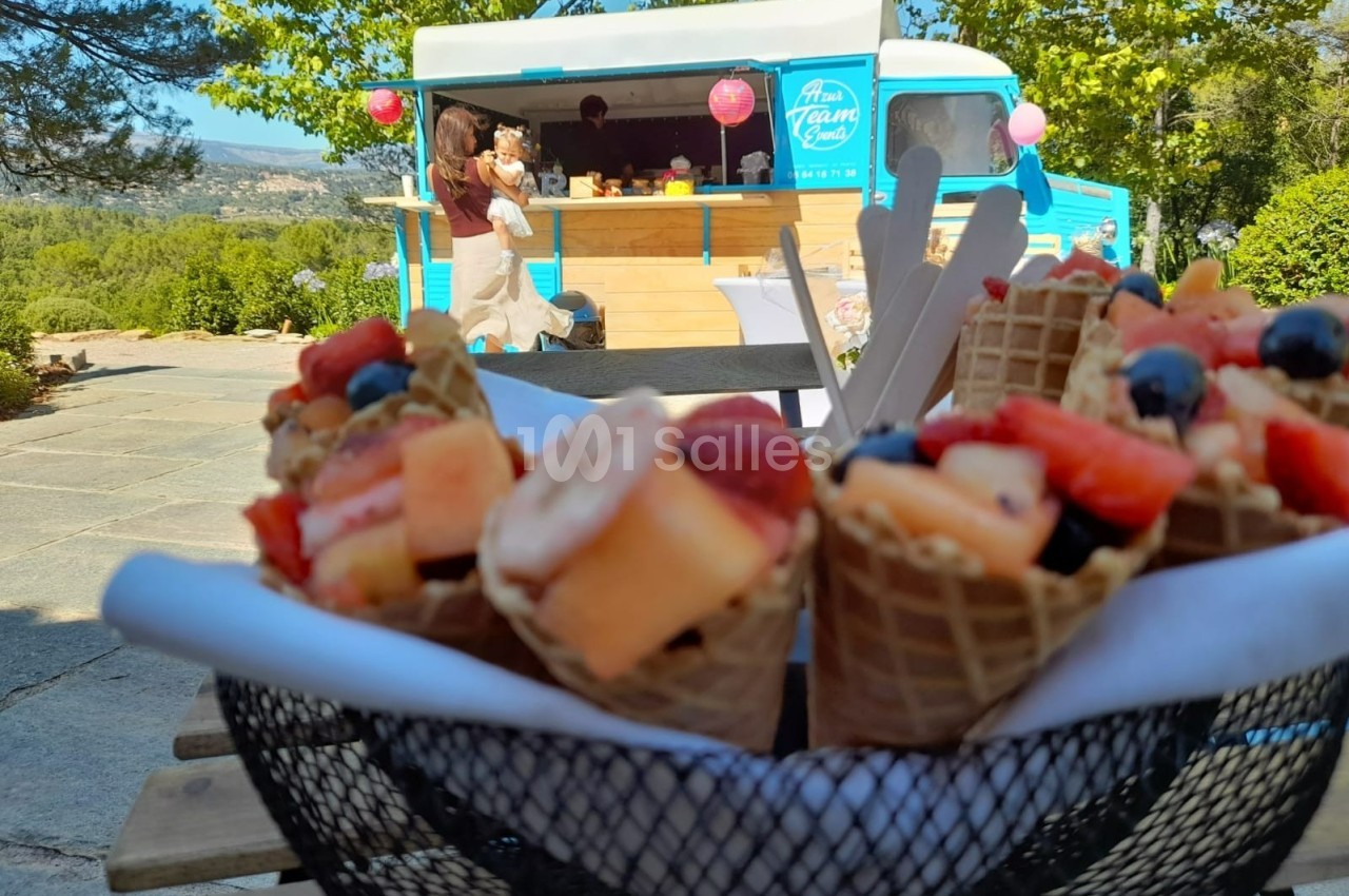Cornets de fruits frais dans un panier, avec un food truck bleu en arrière-plan dans un cadre ensoleillé.