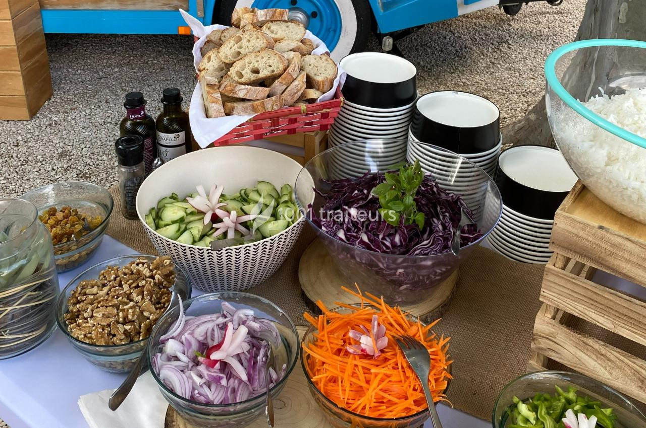 Buffet de salades avec légumes frais, noix, pain tranché et condiments, présenté en extérieur sur une table.
