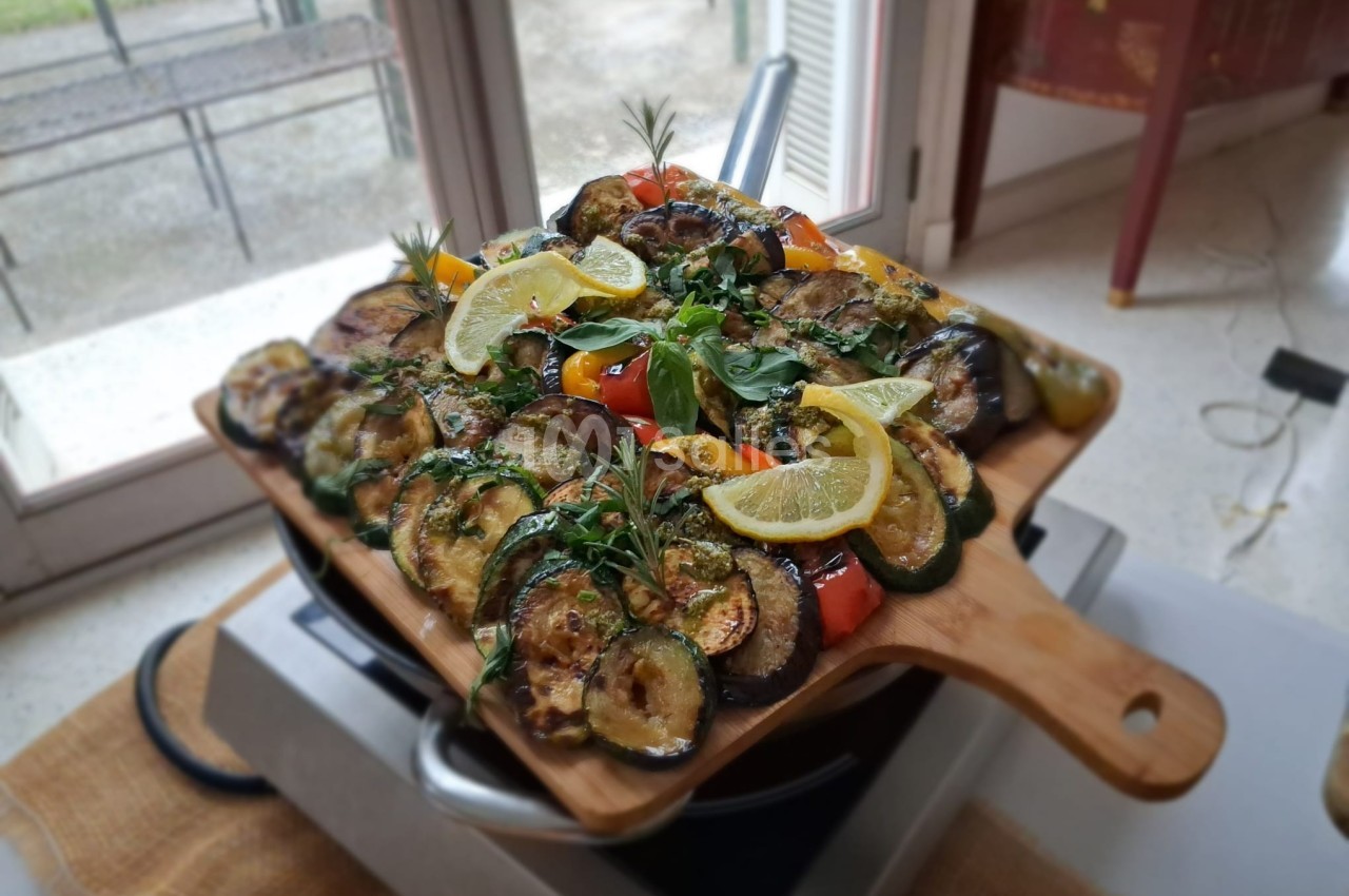Plateau de légumes grillés, incluant courgettes, aubergines, poivrons et rondelles de citron, présenté sur une planche en…