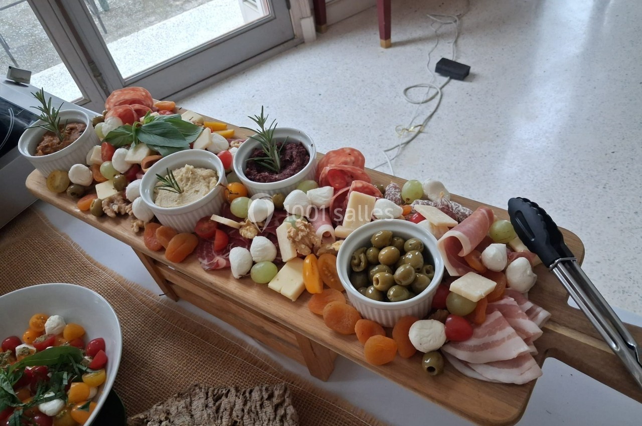 Plateau en bois garni de charcuteries, fromages, olives, fruits secs et dips, présenté sur une table.