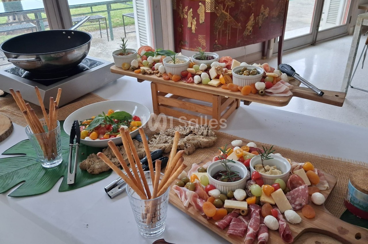 Plateau de charcuterie, fromages, légumes et grissini disposés sur une table dans un cadre lumineux et ouvert.