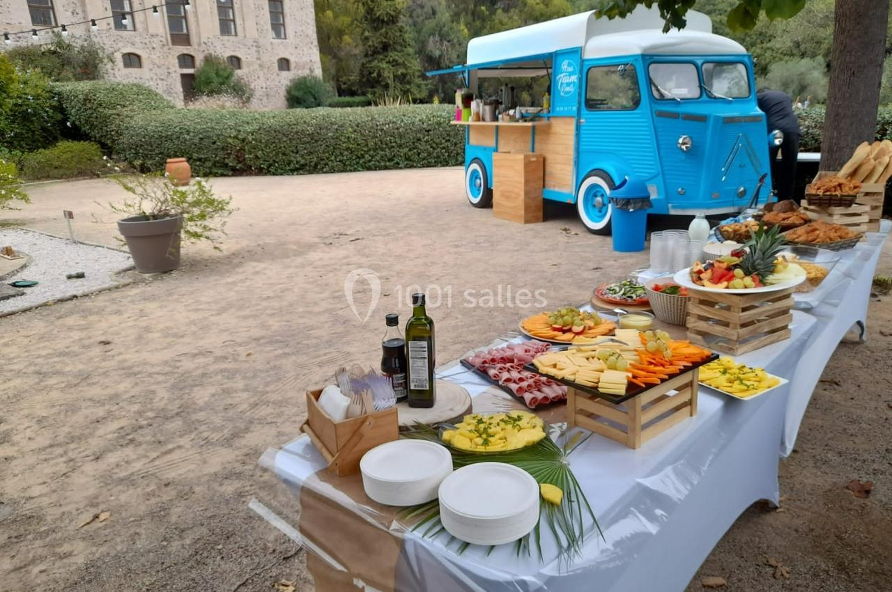 Table dressée avec des plats variés et un food truck bleu en arrière-plan dans un cadre extérieur.