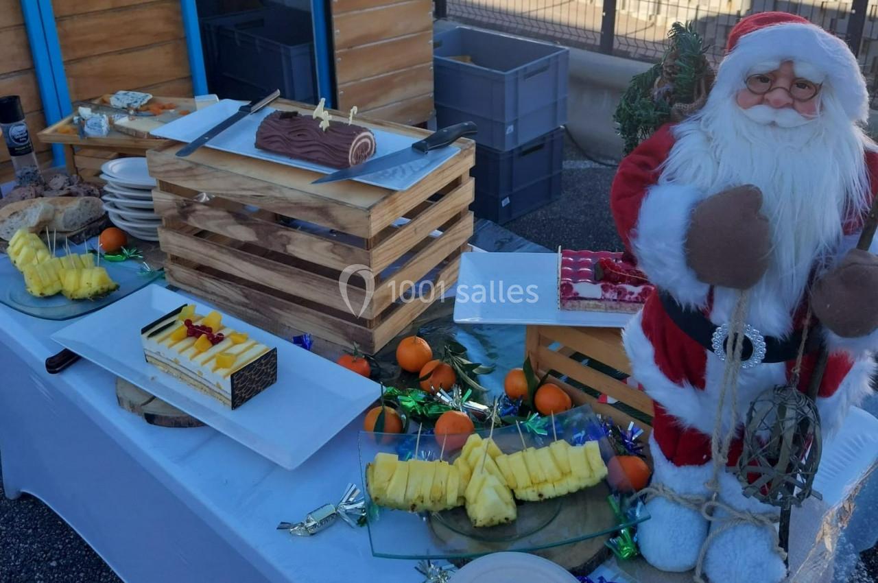 Table garnie de desserts, fruits et décorations de Noël, avec une figurine de Père Noël en premier plan.