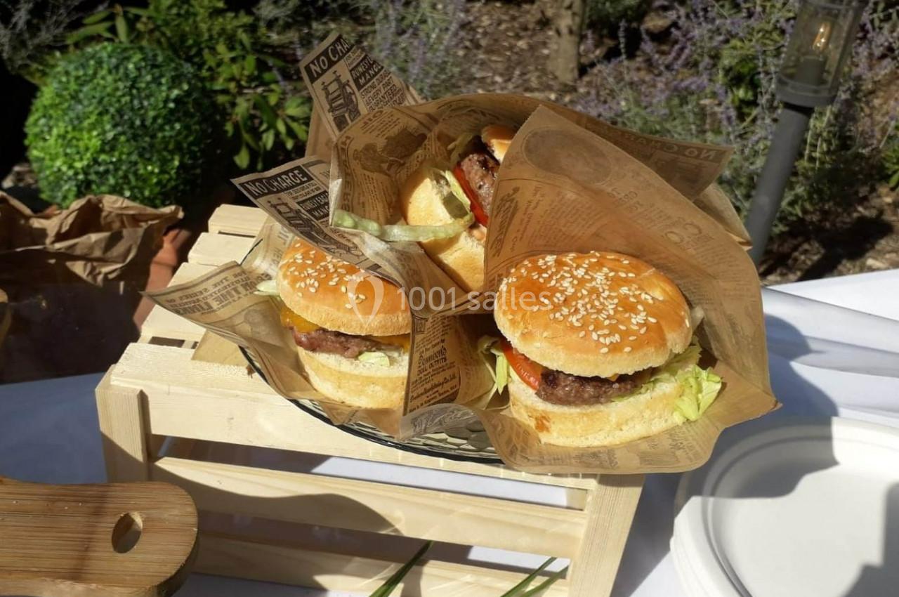 Trois hamburgers garnis de salade, tomate et steak, présentés dans des emballages en papier sur un support en bois.