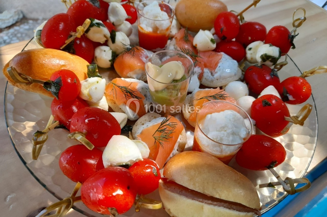 Assortiment d'amuse-bouches avec brochettes de tomates, mozzarella, saumon fumé et mini pains sur un plateau.