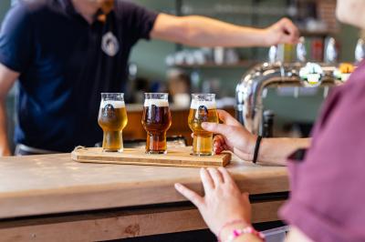 Une personne sert un plateau de dégustation avec trois verres de bière sur un comptoir de bar.