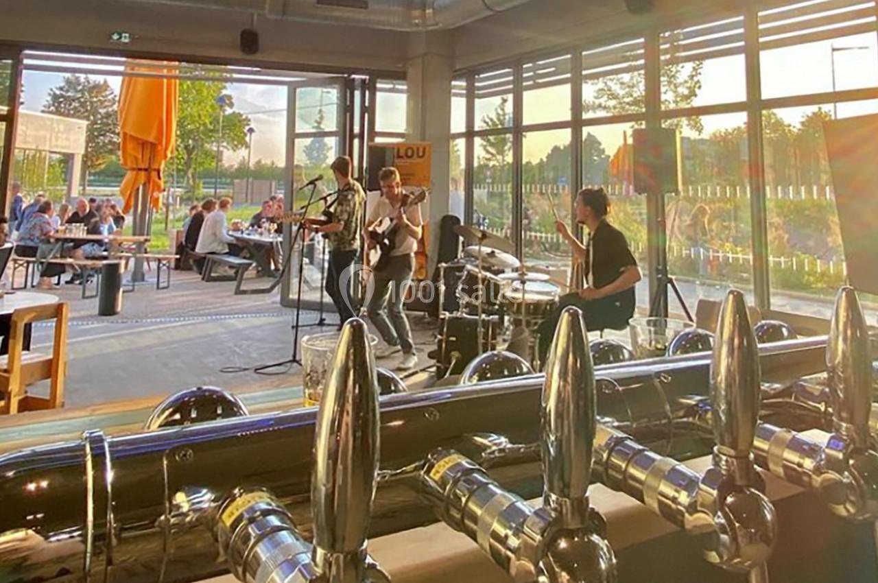 Groupe de musiciens jouant dans un bar lumineux avec des clients assis en terrasse au coucher du soleil.