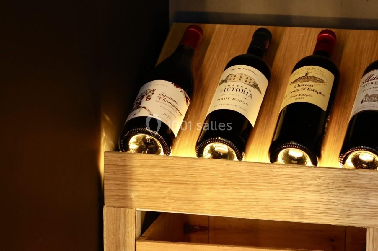 Quatre bouteilles de vin rouge exposées sur un présentoir en bois éclairé, avec une caisse de vin en dessous.