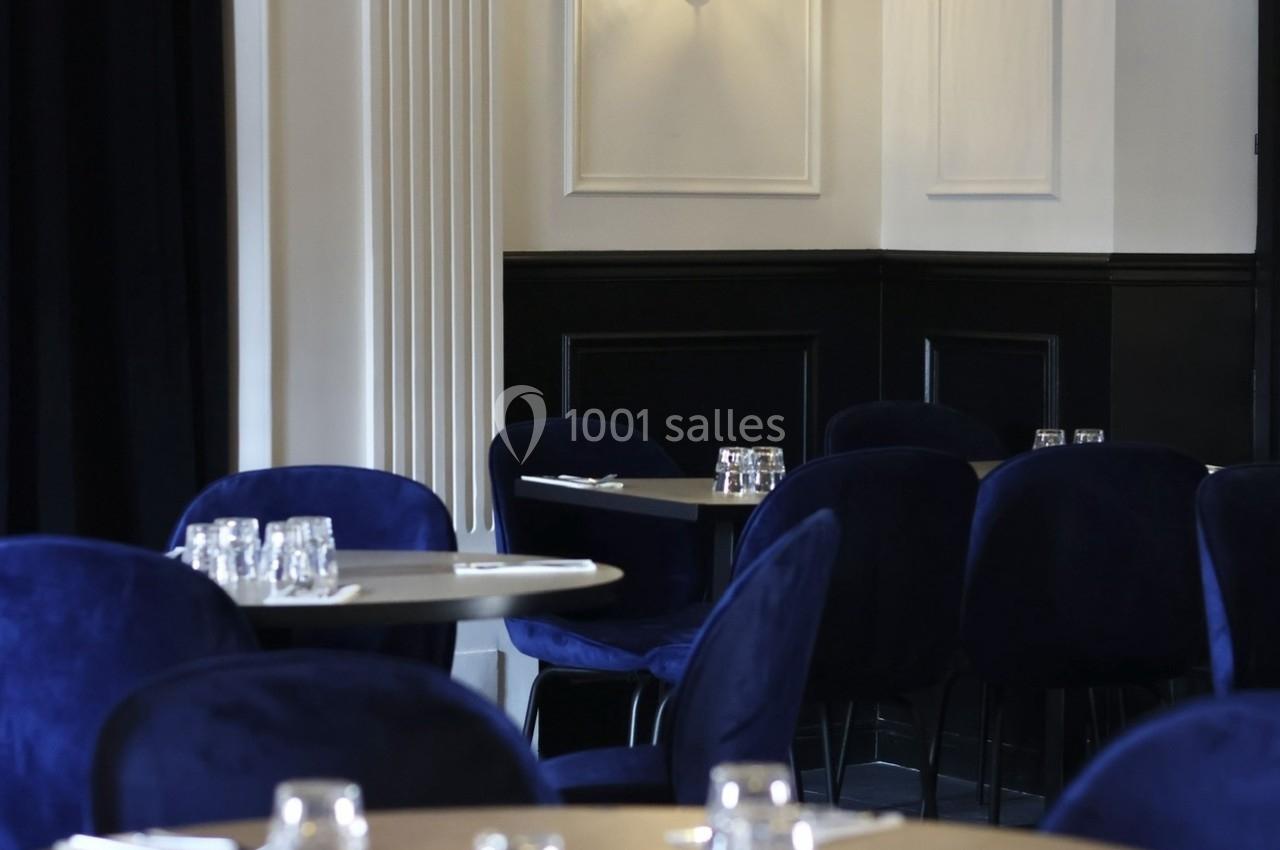 Salle de restaurant élégante avec tables en bois, chaises bleues et éclairage mural discret.