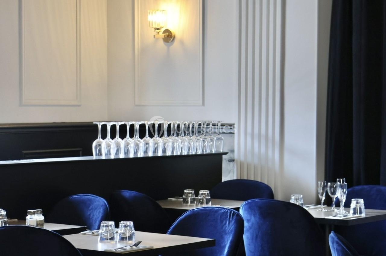 Salle de restaurant élégante avec des chaises bleu velours, des tables dressées et une lumière murale douce.