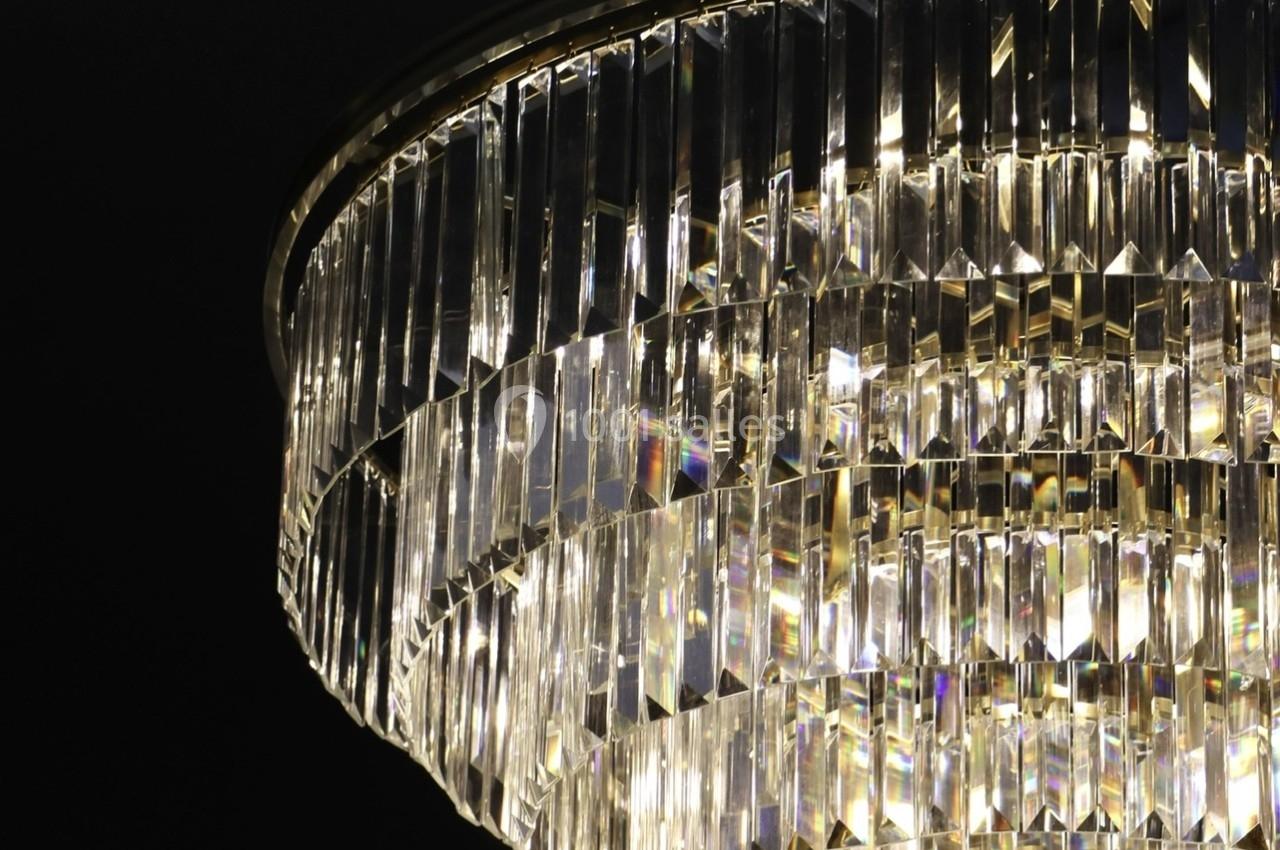 Lustre en cristal suspendu, illuminé, avec des prismes reflétant la lumière sur un fond sombre.