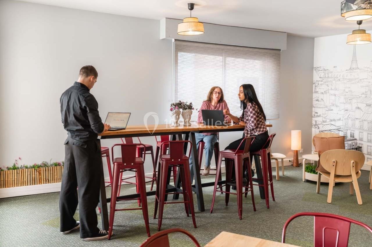 Trois personnes travaillent et discutent autour d'une table haute dans un espace lumineux et aménagé.
