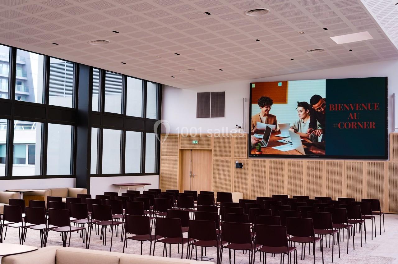 Salle de conférence moderne avec des rangées de chaises vides et un écran affichant ’Bienvenue au Corner’.