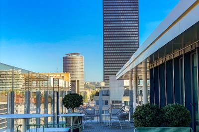 Vue depuis une salle de réunion avec une table, des chaises et une fenêtre donnant sur des immeubles modernes.