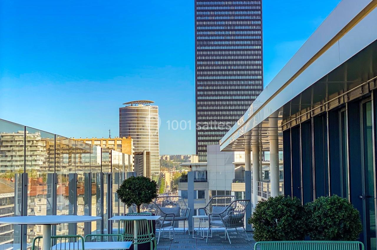 Terrasse aménagée avec mobilier vert, offrant une vue sur des immeubles modernes et un ciel dégagé.