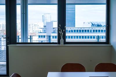 Vue depuis une salle de réunion avec une table, des chaises et une fenêtre donnant sur des immeubles modernes.