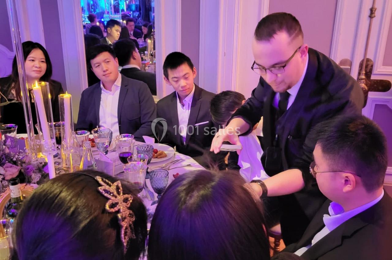 Un magicien réalise un tour de cartes devant des convives assis autour d'une table lors d'un événement festif.