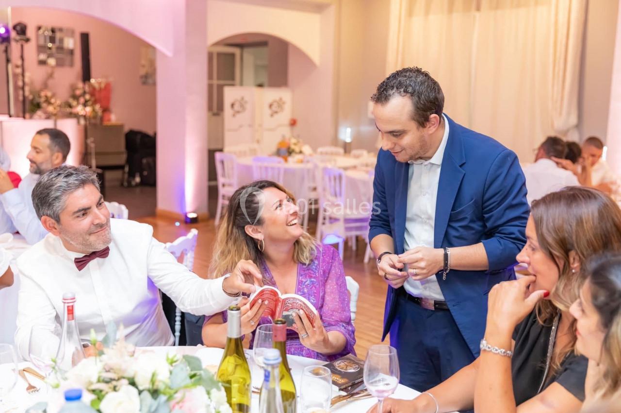 Un magicien réalise un tour de cartes devant des invités assis à une table lors d'une réception festive.