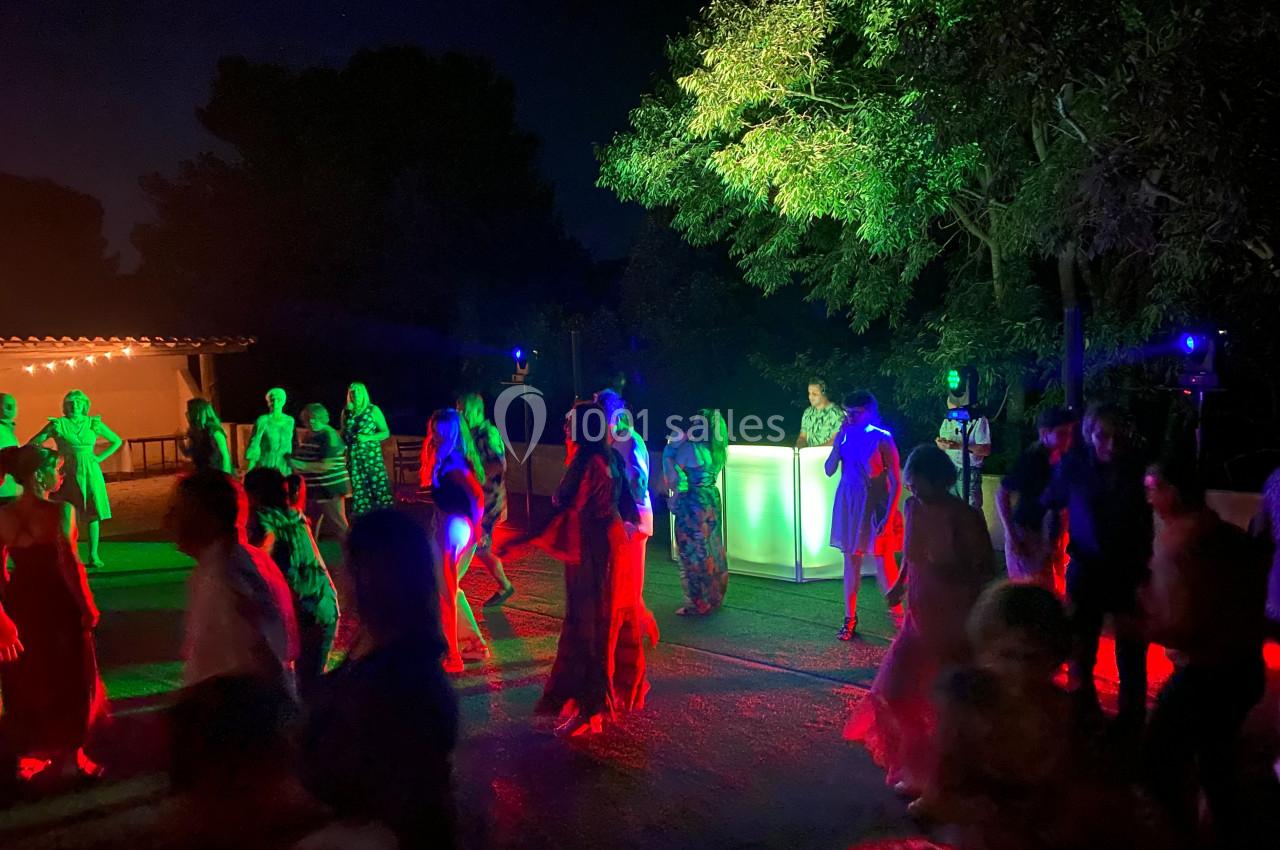 Personnes dansant en extérieur la nuit, éclairées par des lumières colorées près d'un bar lumineux.
