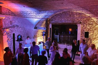 Console de DJ éclairée en violet et jaune, entourée de plantes et d'équipements audio dans une salle sombre.