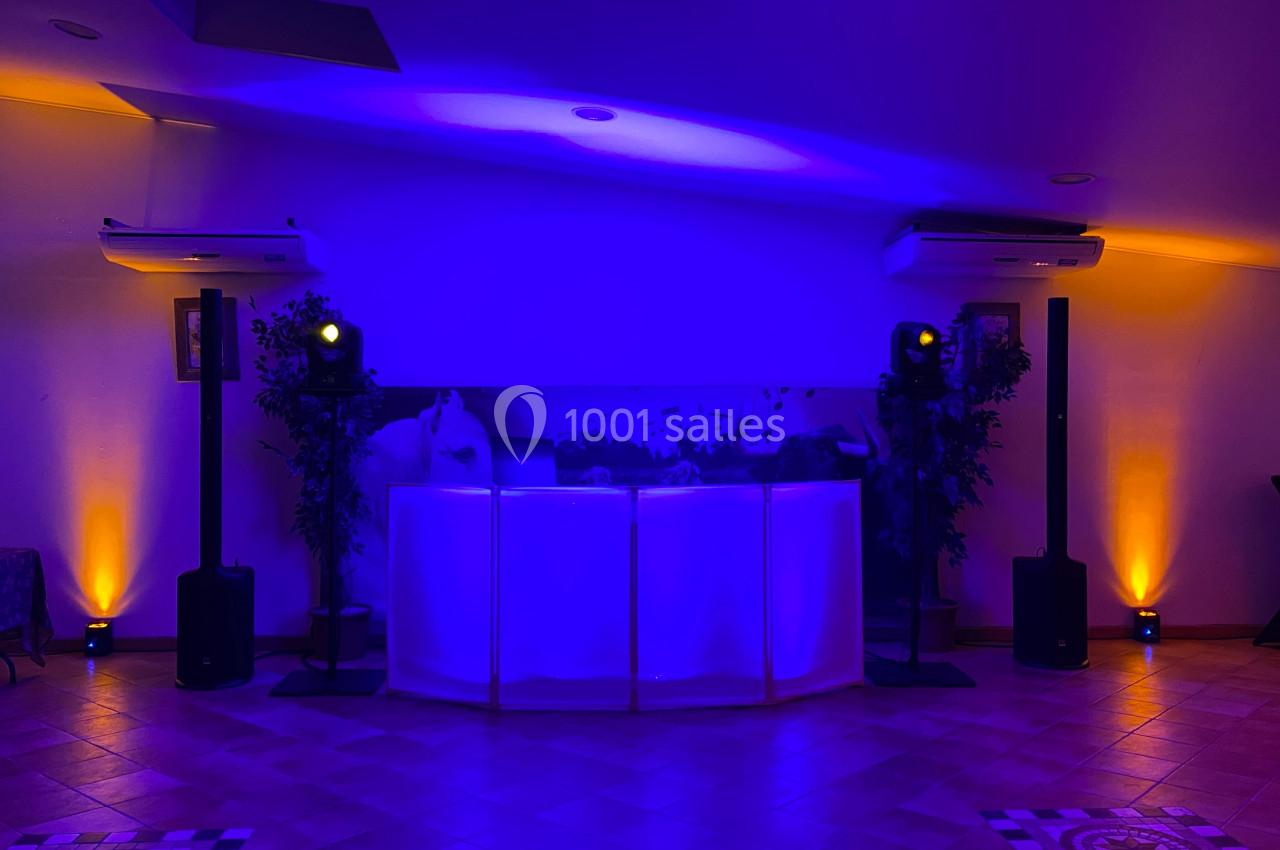 Console de DJ éclairée en violet et jaune, entourée de plantes et d'équipements audio dans une salle sombre.