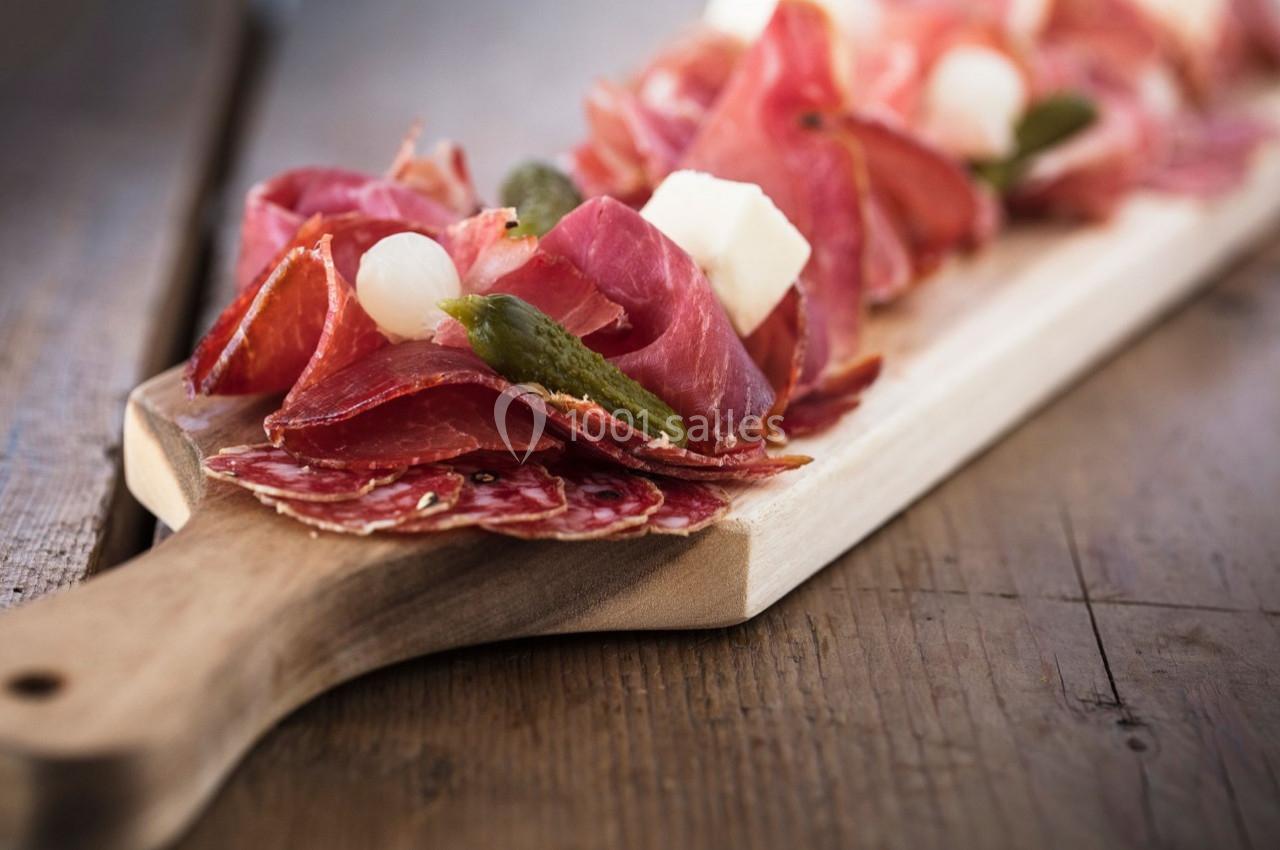 Planche en bois garnie de charcuterie, cornichons, oignons marinés et cubes de fromage.