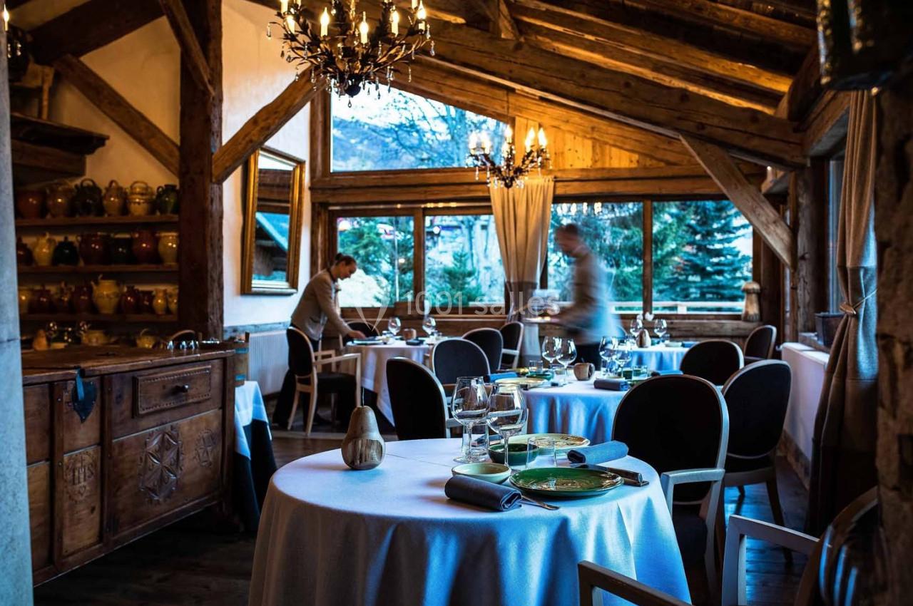 Salle de restaurant chaleureuse avec tables dressées, décor en bois et grandes fenêtres donnant sur un paysage extérieur.