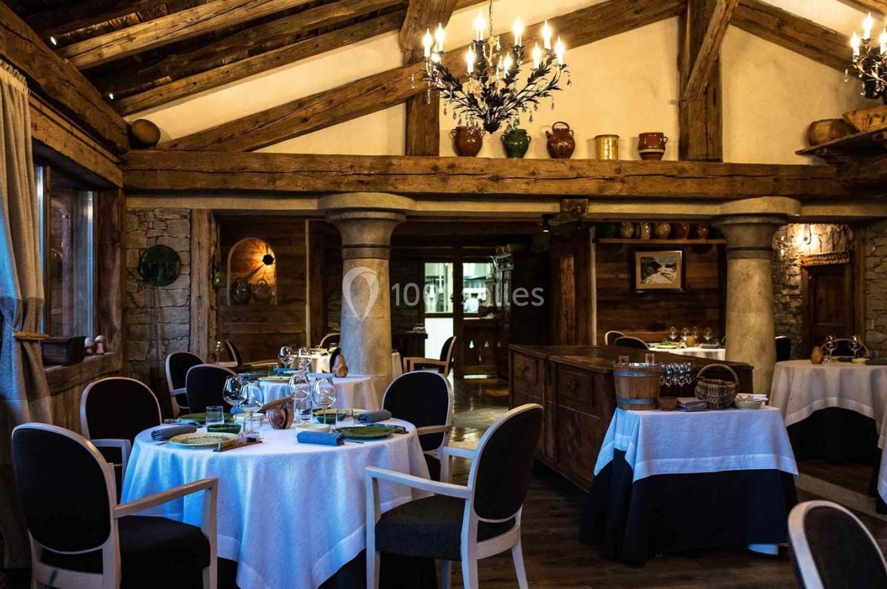 Salle de restaurant rustique avec poutres apparentes, tables dressées et ambiance chaleureuse.