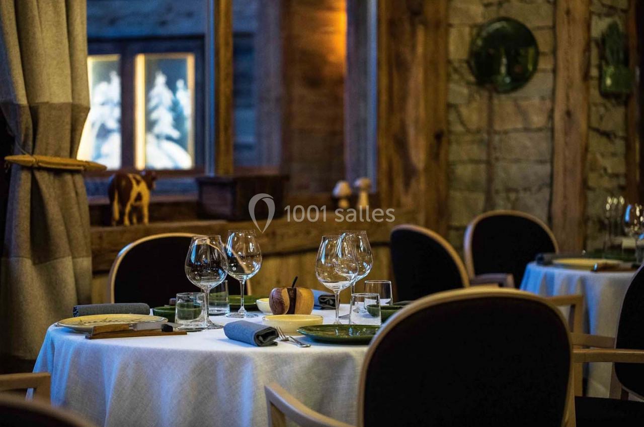 Salle de restaurant élégante avec tables dressées, nappes blanches, verres à pied et ambiance chaleureuse en bois.