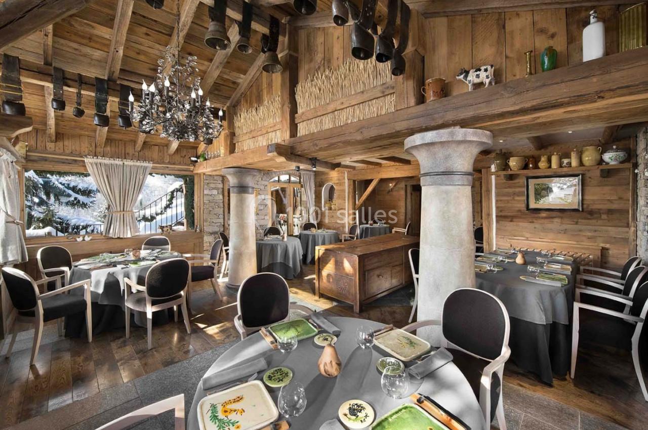 Salle de restaurant chaleureuse en bois avec tables dressées, grandes fenêtres et vue sur un paysage enneigé.