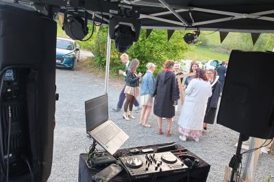 Un homme s'exprime au micro devant un public rassemblé dans une cour extérieure entourée de végétation.