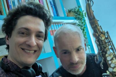 Un homme s'exprime au micro devant un public rassemblé dans une cour extérieure entourée de végétation.