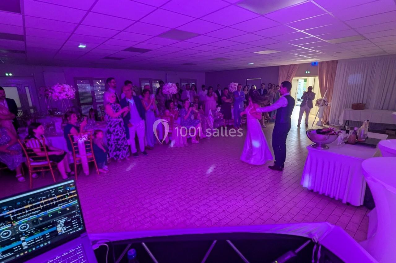 Un couple danse au centre d'une salle éclairée de lumières violettes, entouré d'invités assis et debout.