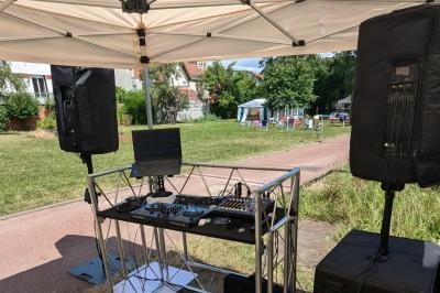 Un homme s'exprime au micro devant un public rassemblé dans une cour extérieure entourée de végétation.