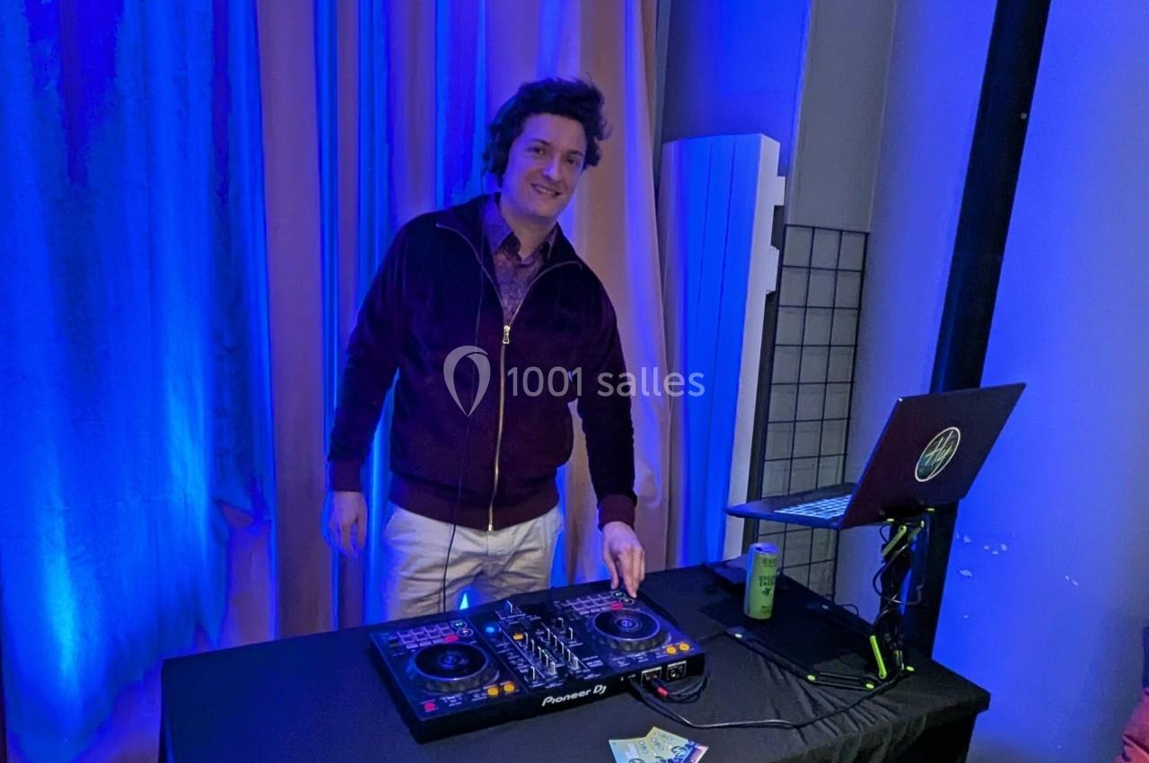 Un DJ souriant mixe de la musique sur une table de mixage dans un espace éclairé par des lumières bleues.