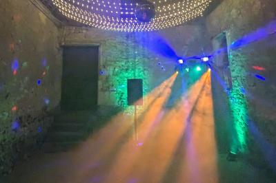 Un homme s'exprime au micro devant un public rassemblé dans une cour extérieure entourée de végétation.