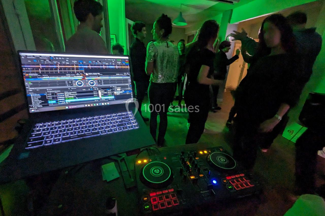 Des personnes dansent dans une pièce éclairée de lumières vertes, avec une table de mixage et un ordinateur au premier plan.