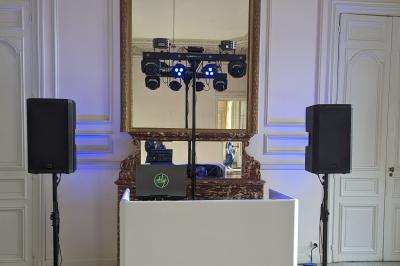 Un homme s'exprime au micro devant un public rassemblé dans une cour extérieure entourée de végétation.