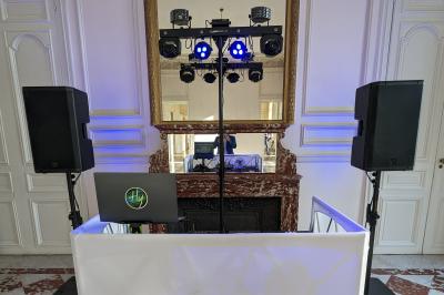 Un homme s'exprime au micro devant un public rassemblé dans une cour extérieure entourée de végétation.