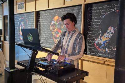 Un DJ mixe de la musique sur une table de mixage dans un espace intérieur avec des œuvres d'art en arrière-plan.