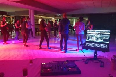 Groupe de personnes dansant dans une salle éclairée par des lumières colorées, avec une table de mixage au premier plan.