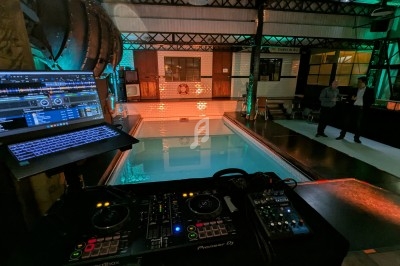 Poste de DJ avec platines et ordinateur portable installé près d'une piscine intérieure dans un espace industriel éclairé.