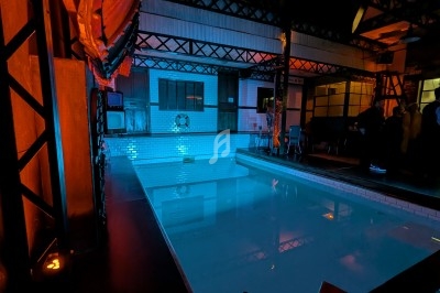 Piscine intérieure vide éclairée par des lumières colorées dans un environnement industriel.