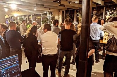 Groupe de personnes rassemblées dans un espace intérieur moderne, avec un ordinateur de DJ visible au premier plan.