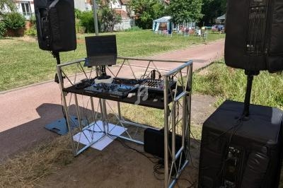 Table de mixage et équipements audio sous une tente, installés en extérieur sur un chemin bordé de verdure.